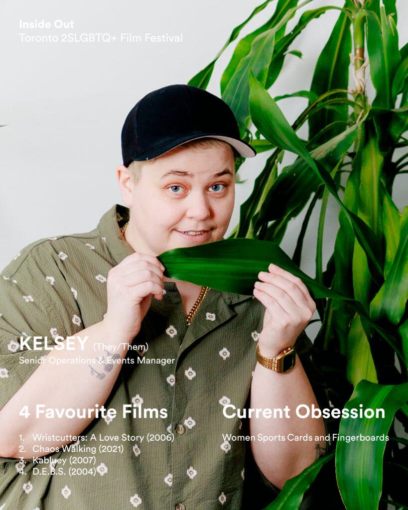 A person wearing a black cap and light shirt smiles while holding a large green leaf.