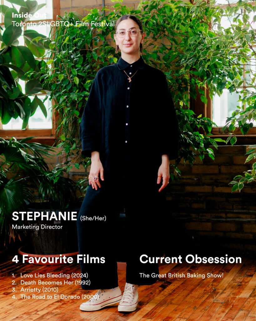 A person, wearing black clothes and white sneakers, stands indoors by leafy plants.