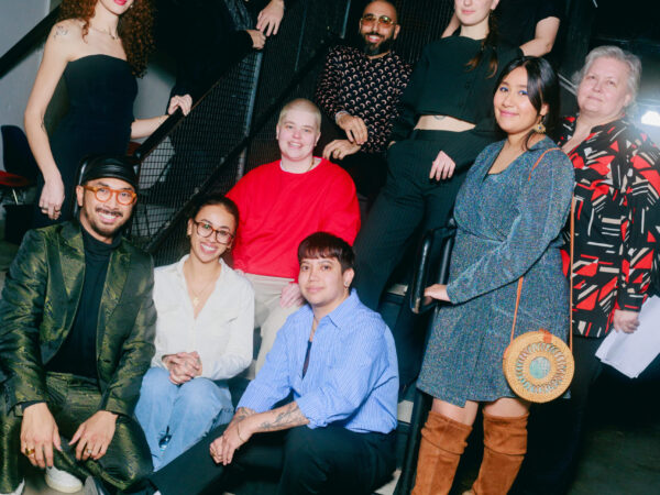 A group of eleven people pose together on and around a staircase indoors, smiling at the camera. The lighting is bright, and everyone is dressed in stylish, casual to semi-formal attire.
