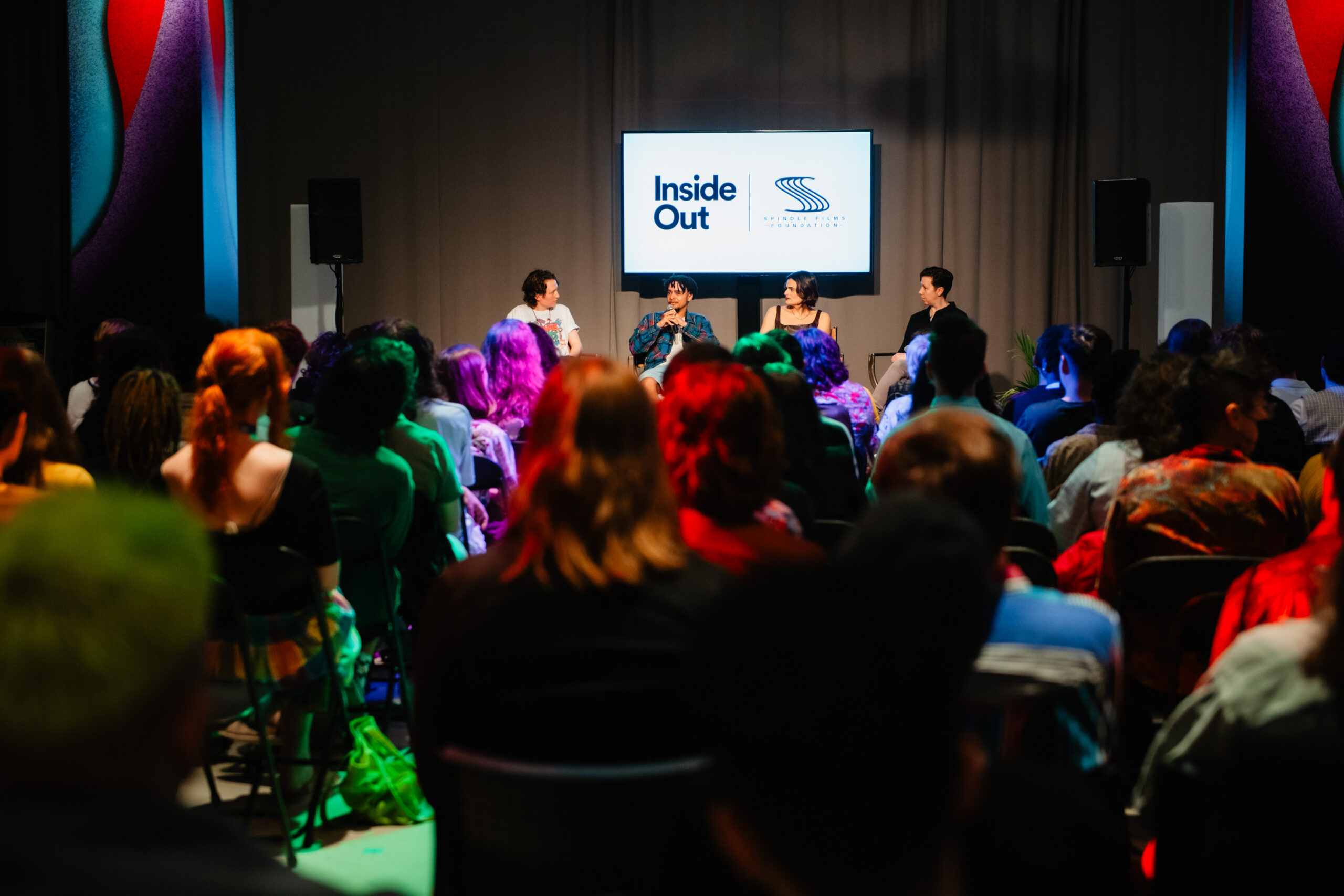 A crowd full of people looking at the stage of four panelists speaking. A screen in the back that reads Inside Out and Spindle Films Foundation.