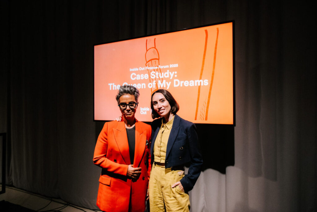 Two people stand in front of a screen displaying "Case Study: The Queen of My Dreams" at a film forum event. One person wears an orange blazer; the other wears a dark blazer and yellow shirt. Both are smiling.