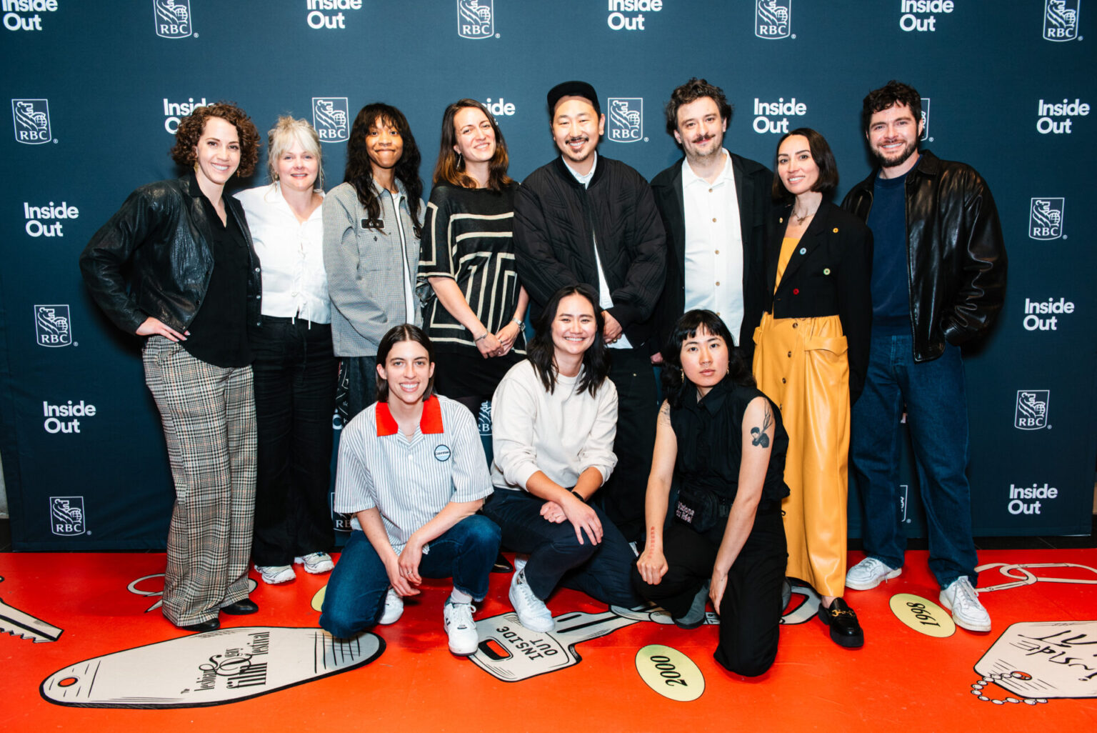 A group of eleven people pose together, smiling, in front of a blue backdrop with "Inside Out" and "RBC" logos. Some are standing, others are kneeling, dressed in casual and semi-formal attire.