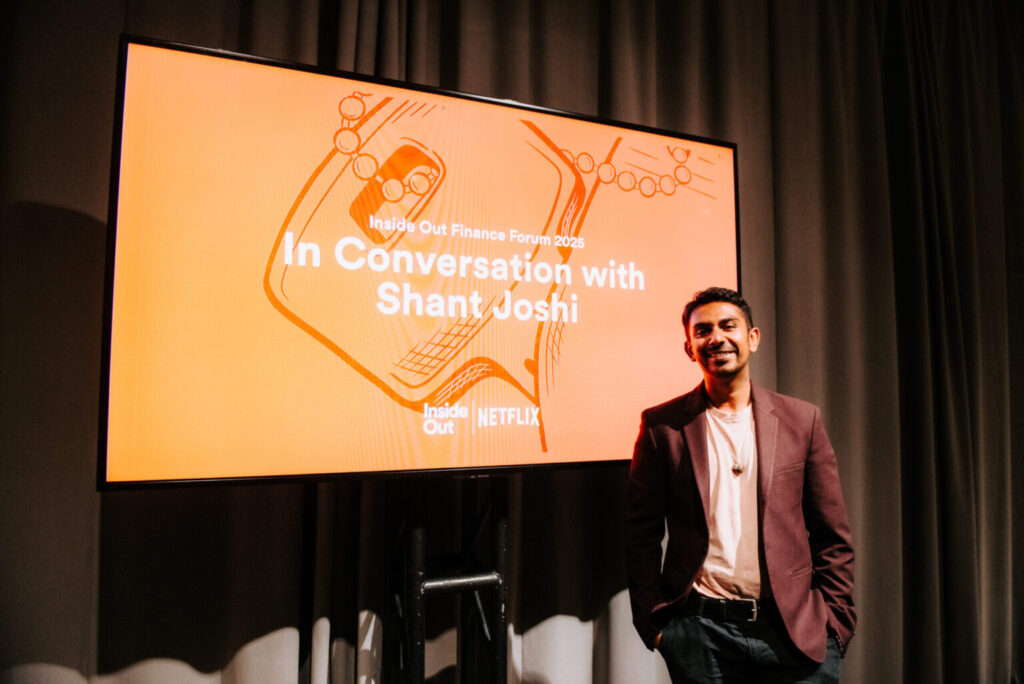 A man in a maroon blazer stands smiling next to a large screen displaying the text “In Conversation with Shant Joshi” at the Inside Out Finance Forum 2023, with Netflix and Inside Out logos visible.